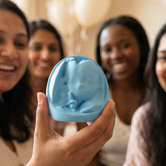 A pregnant woman holds up a light blue 3D printed keepsake of her unborn baby, with family and friends at a baby shower.