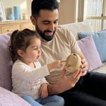 A father and daughter sitting on a couch in a living room, looking at and holding a 3D print keepsake, which represents her size and development when she was in her mother's womb.