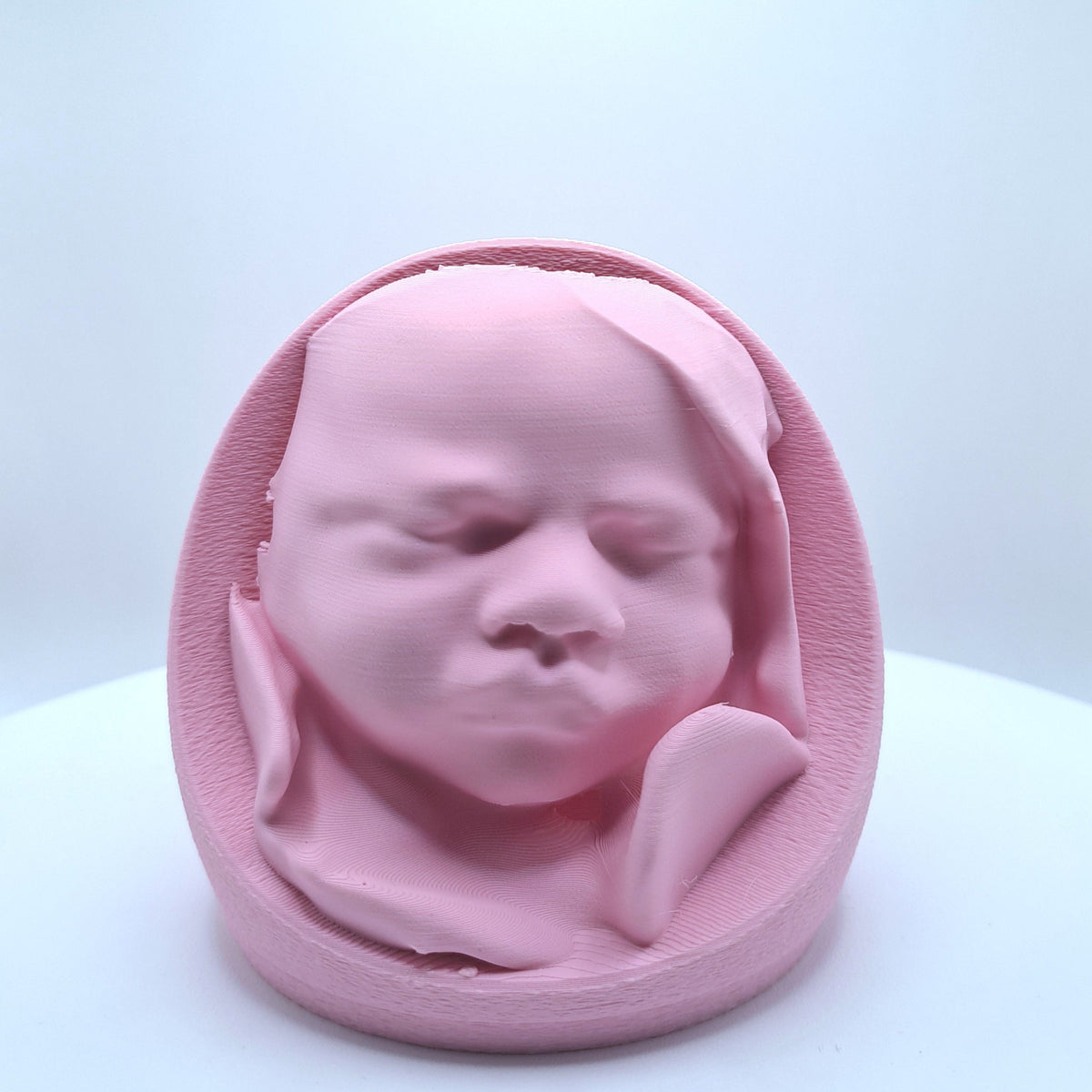 A light pink 3D printed replica of a sleeping newborn baby's head in a belly.